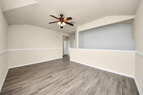 a view of an empty room with wooden floor and a ceiling fan