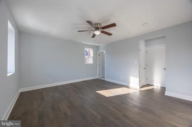 an empty room with wooden floor ceiling fan and windows