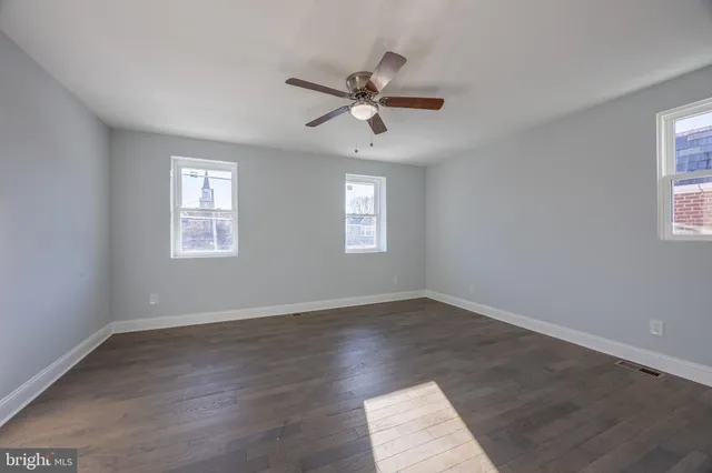 an empty room with wooden floor windows and fan