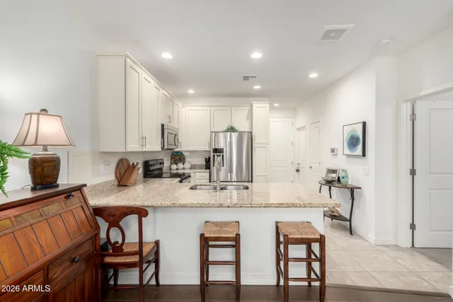a kitchen with kitchen island granite countertop a dining table chairs refrigerator and cabinets