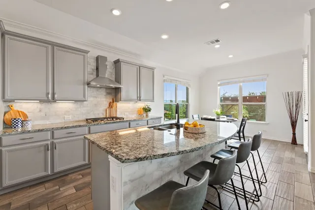 a kitchen with stainless steel appliances granite countertop a stove top oven a sink a dining table and chairs with wooden floor