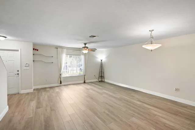 an empty room with wooden floor chandelier and windows