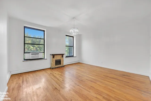 an empty room with wooden floor fireplace and windows