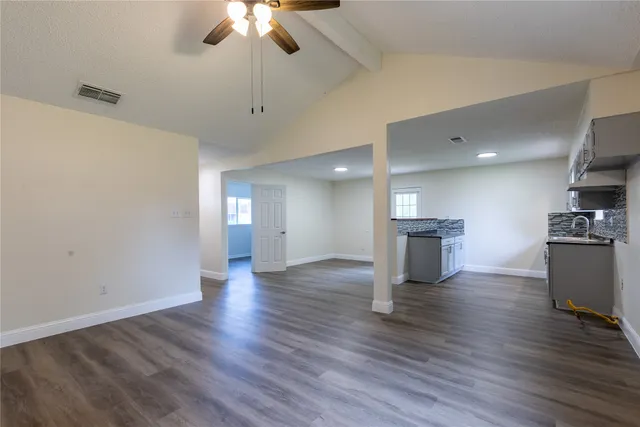 a view of empty room with wooden floor and kitchen