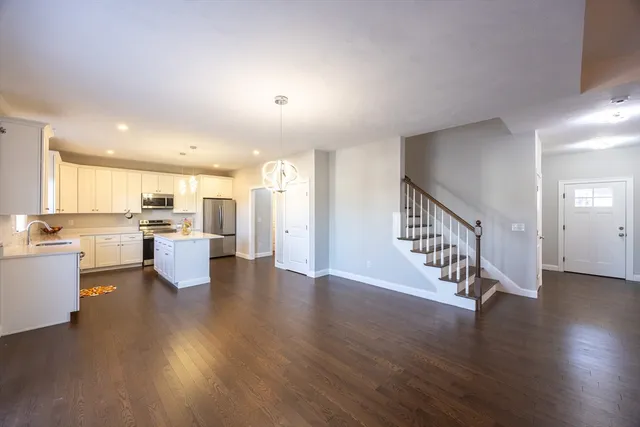 a view of an empty room and kitchen with wooden floor