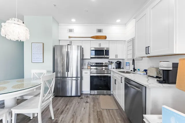 a kitchen with kitchen island granite countertop stainless steel appliances a refrigerator a stove top oven and a dining table with wooden floor