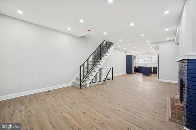 a view of an empty room with wooden floor stairs and a way to kitchen