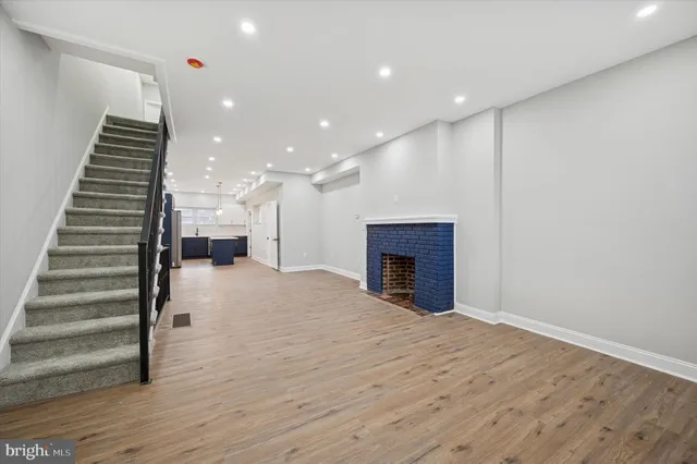 a view of an empty room with wooden floor staircase and a kitchen