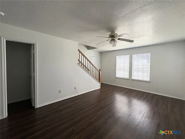 an empty room with wooden floor chandelier fan and windows