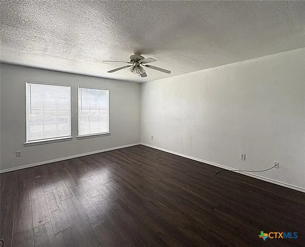 an empty room with wooden floor chandelier fan and windows