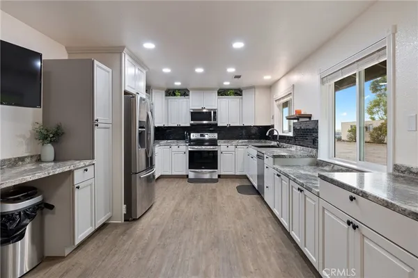 a kitchen with stainless steel appliances granite countertop a refrigerator a stove top oven a sink dishwasher and white cabinets with wooden floor
