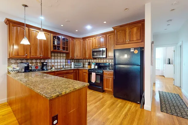 a kitchen with stainless steel appliances granite countertop a refrigerator a sink a stove and a wooden cabinets