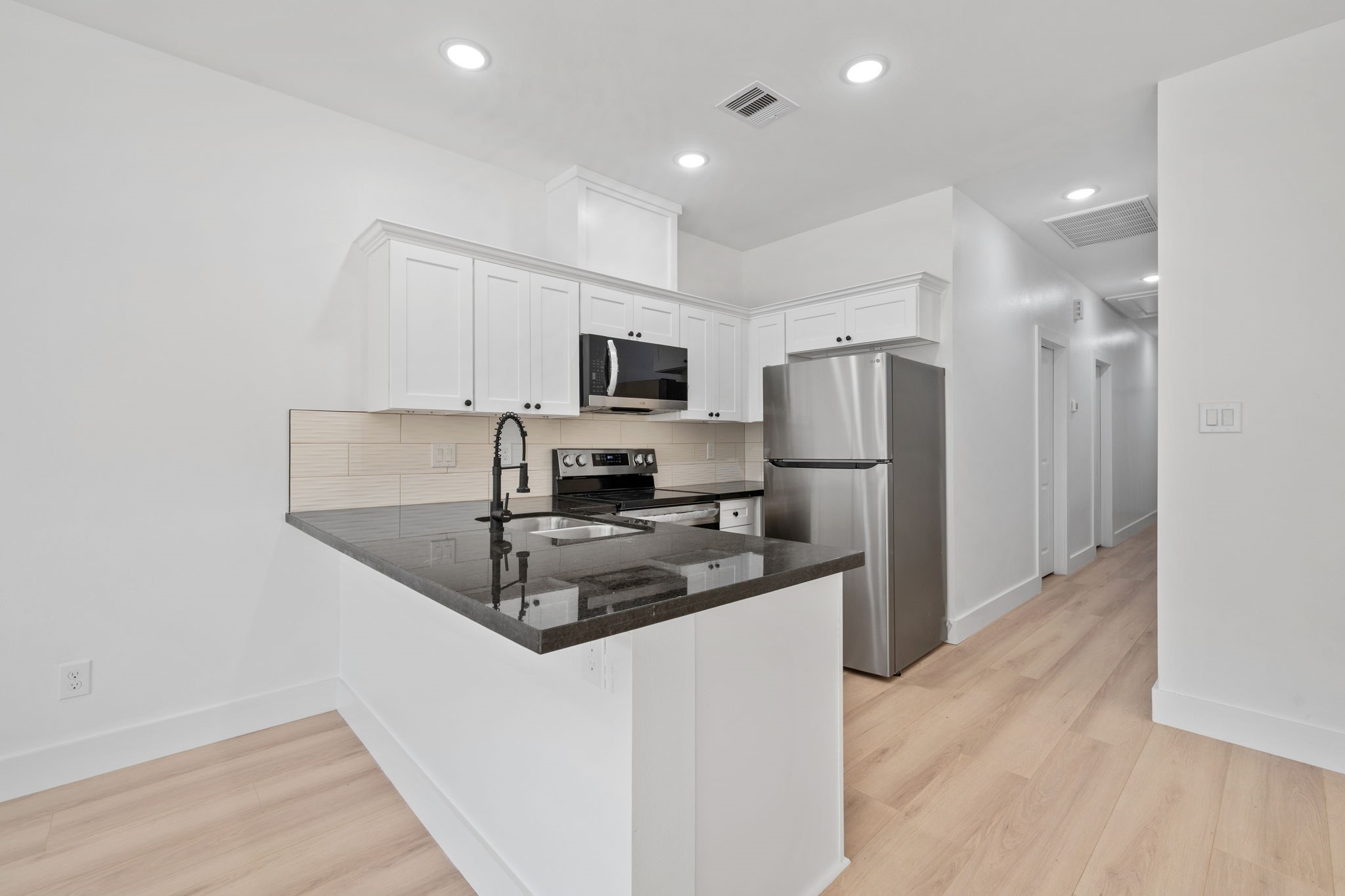 8410 Sunnyhill Street Houston, TX 77088 - Photo 12 of 20 a kitchen with a refrigerator a microwave a sink and white cabinets
