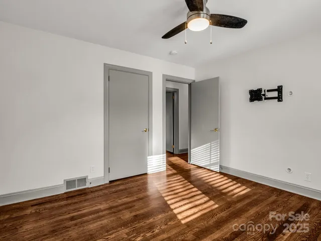 a view of an empty room with wooden floor and a ceiling fan