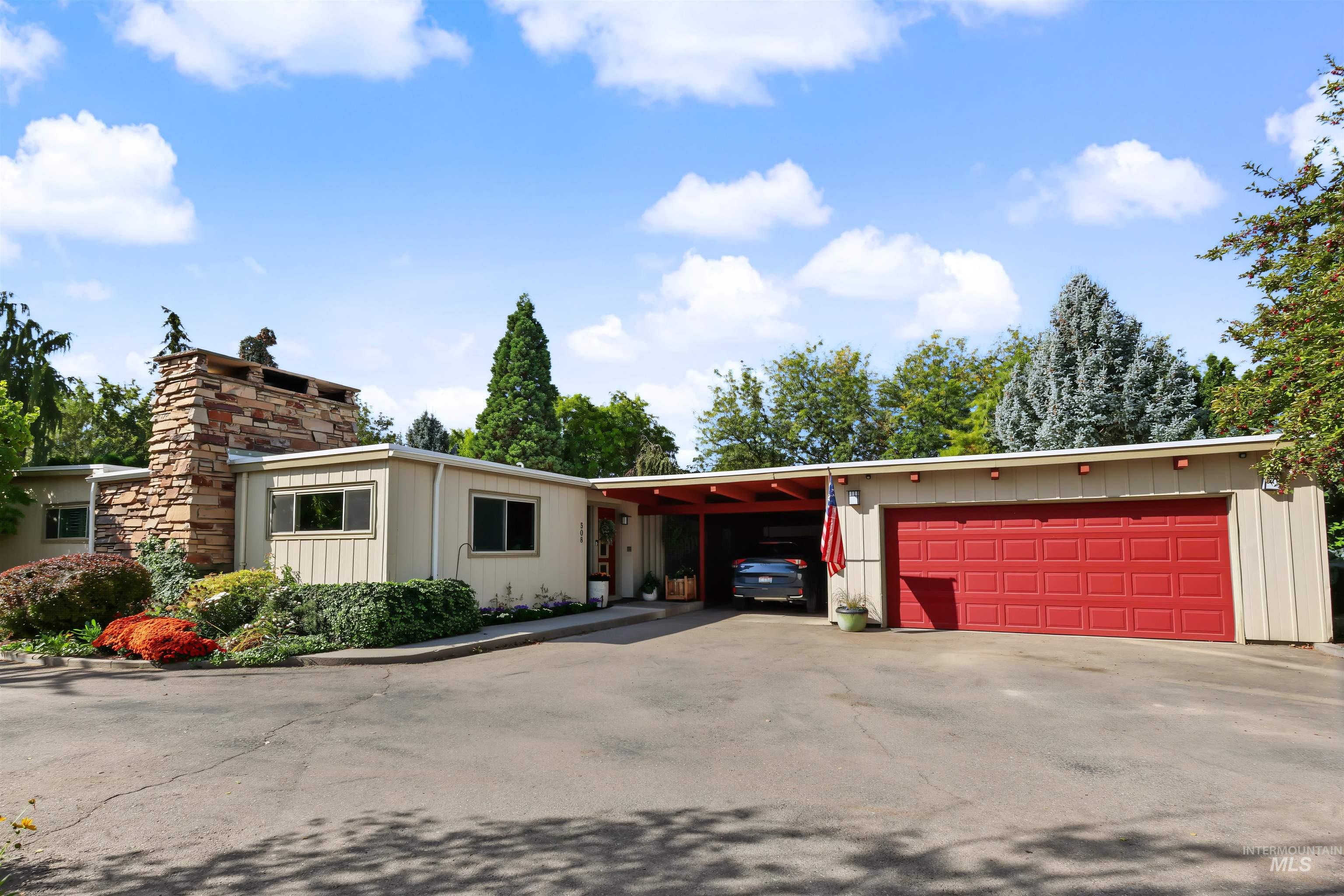 508 East Elm Avenue Parma, ID 83660 - Photo 1 of 50 Mid-century modern exterior with a stone chimney, a red garage door, and a covered carport