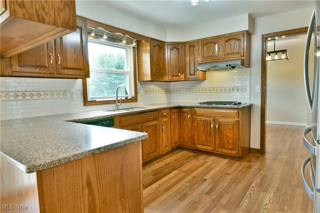 2153 Stillwagon Road Southeast Warren, OH 44484 - Photo 16 of 50 Kitchen featuring a sink, under cabinet range hood, brown cabinetry, and tasteful backsplash