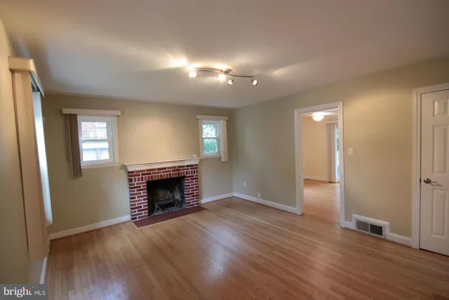 an empty room with wooden floor fireplace and windows