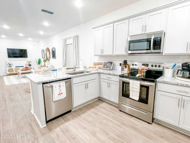 a kitchen with stainless steel appliances granite countertop white cabinets a sink a window and a microwave