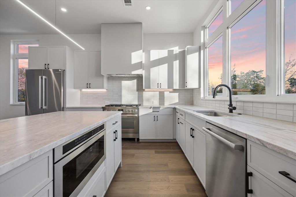 4101 Menchaca Road, Unit 102 Austin, TX 78704 - Photo 2 of 14 Sun-filled kitchen with a spacious island, white cabinetry, and large windows revealing a vibrant sunset.