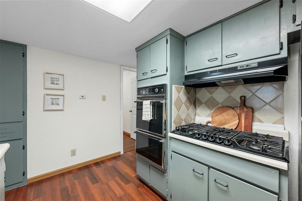 4610 South 1st Street Austin, TX 78745 - Photo 16 of 23 Kitchen featuring black appliances, under cabinet range hood, dark wood finished floors, decorative backsplash, and baseboards