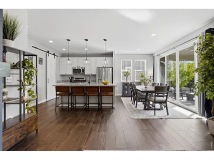 a open kitchen with stainless steel appliances granite countertop a stove top oven a refrigerator a dining table and chairs with wooden floor