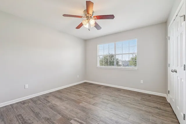 an empty room with wooden floor chandelier fan and windows