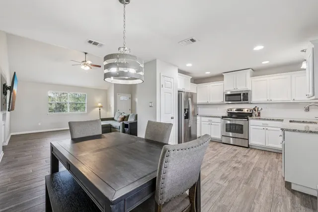 a kitchen with stainless steel appliances granite countertop a stove a refrigerator a kitchen island a sink white cabinets and couches with wooden floor