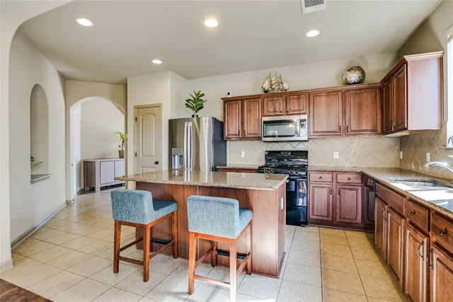 a kitchen with stainless steel appliances granite countertop a stove top oven a sink dishwasher a dining table and chairs with wooden floor