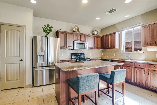 a kitchen with stainless steel appliances granite countertop a refrigerator a stove a sink a dining table and chairs