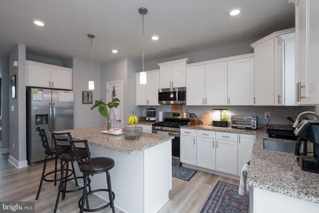 a kitchen with a refrigerator a stove a sink a dining table and chairs with wooden floor