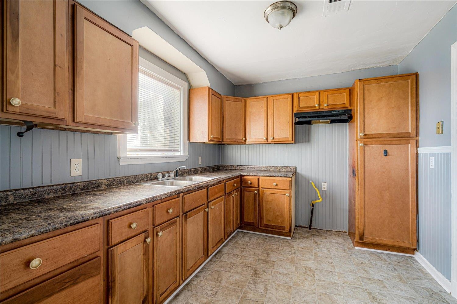 1114 Brownlee Road Memphis, TN 38116 - Photo 18 of 32 Kitchen with wainscoting, brown cabinetry, dark countertops, under cabinet range hood, and wooden walls