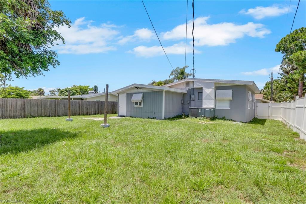 11360 Hunting Road Bonita Springs, FL 34135 - Photo 16 of 27 Expansive grassy backyard featuring a wood privacy fence, white vinyl fencing, mature trees, and a single-story residence with a light gray exterior