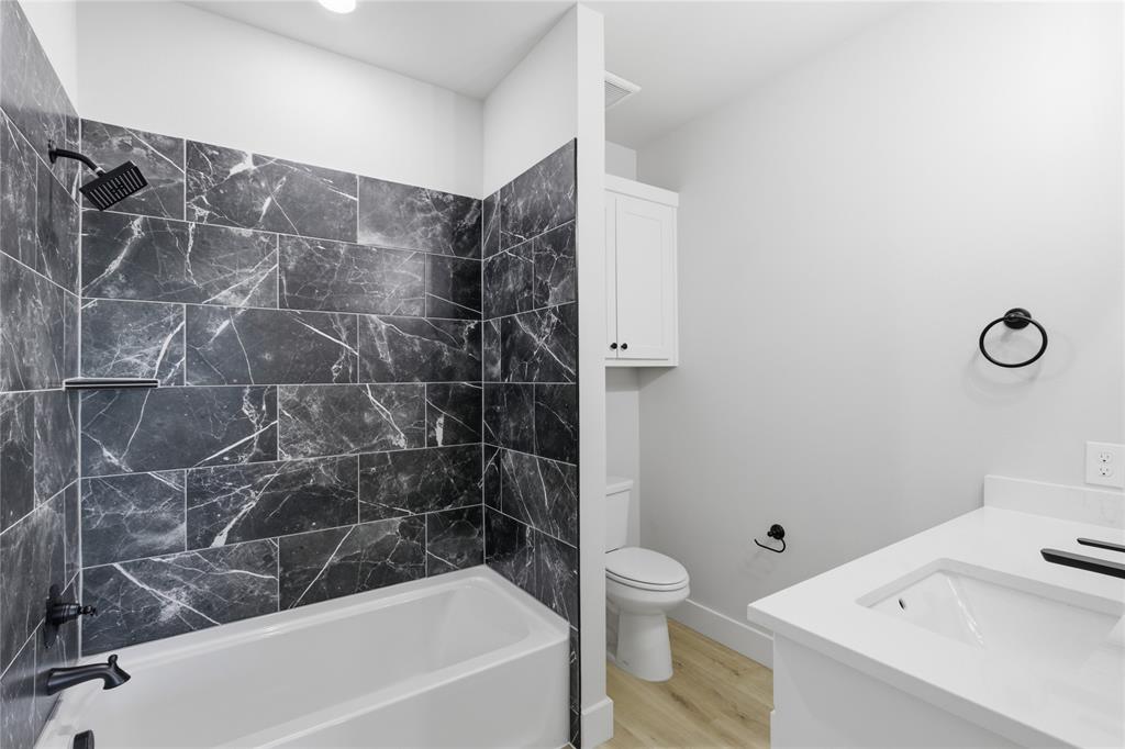 713 Anne Road Van Alstyne, TX 75495 - Photo 15 of 29 Bathroom featuring a white bathtub, dark marbled tile shower surround, matte black shower fixtures, a white vanity with an integrated sink and white countertop, and wood-finish flooring