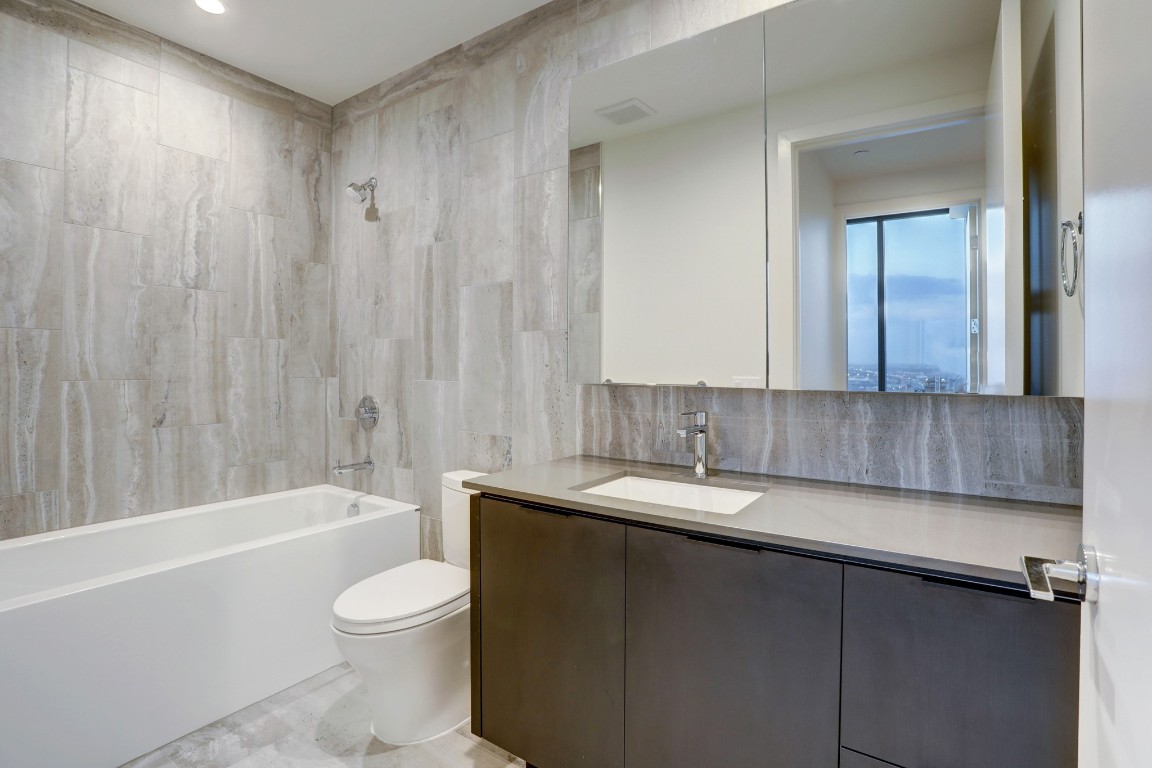 44 East Avenue, Unit 4203 Austin, TX 78701 - Photo 25 of 26 a bathroom with a granite countertop bathtub sink vanity mirror and toilet