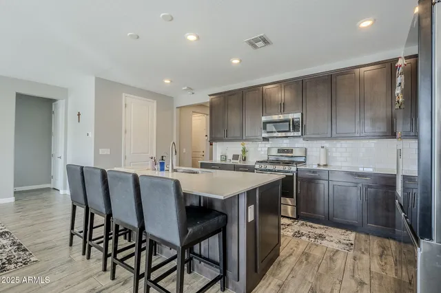 a kitchen with stainless steel appliances granite countertop a stove top oven a refrigerator a sink and chairs