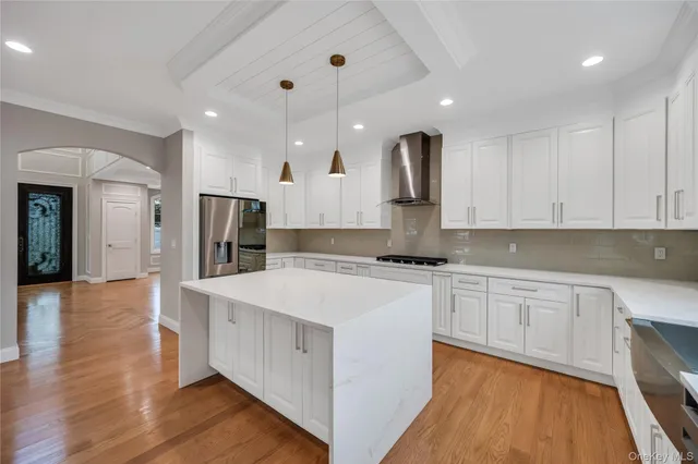 a large kitchen with stainless steel appliances kitchen island a stove a sink a refrigerator and white cabinets with wooden floor