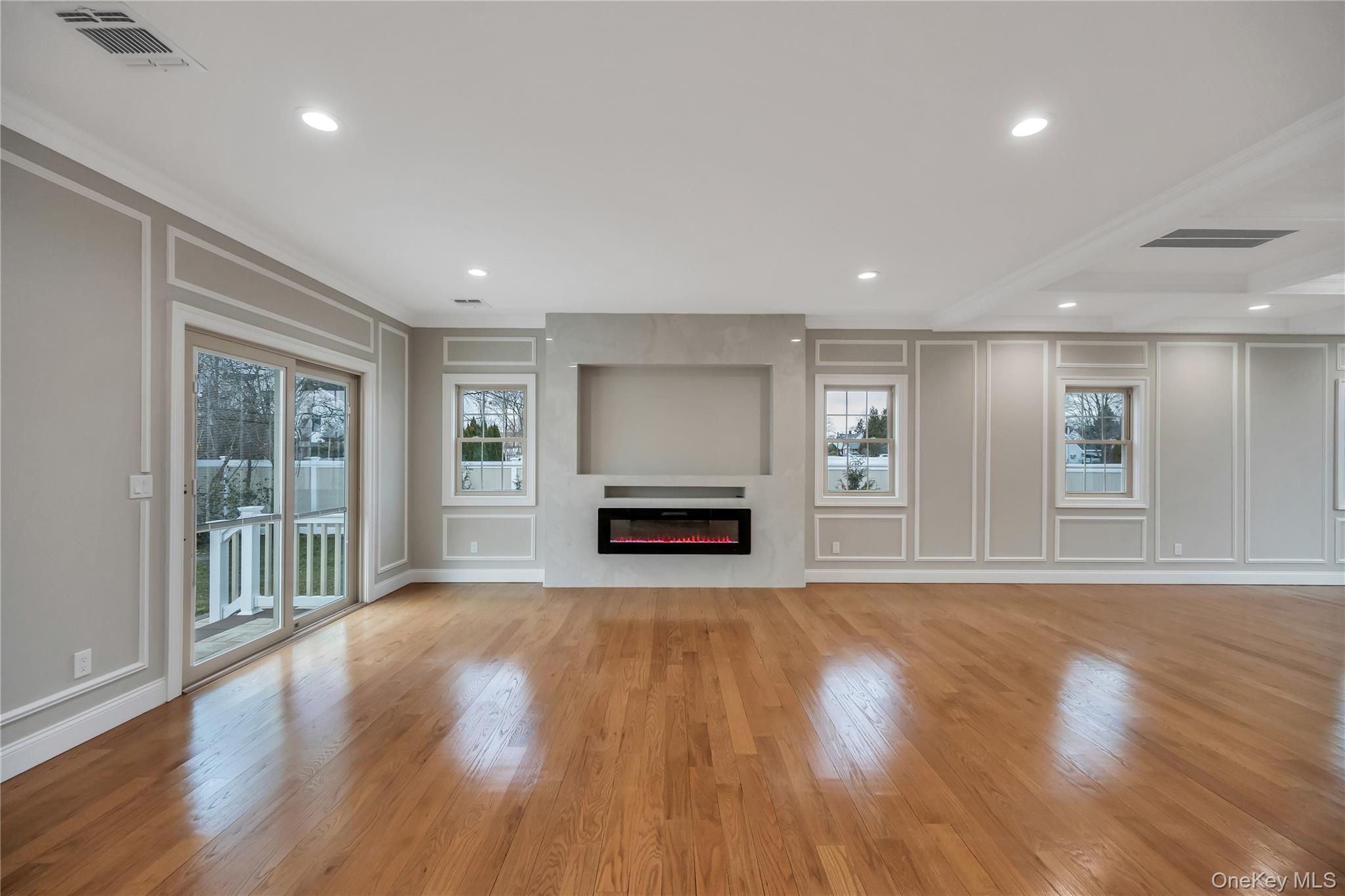 319 Blacksmith Road Levittown, NY 11756 - Photo 6 of 16 Unfurnished living room featuring a decorative wall, crown molding, light wood finished floors, a glass covered fireplace, and recessed lighting