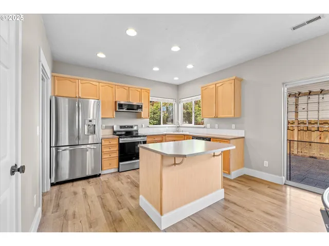 a kitchen with stainless steel appliances granite countertop a refrigerator a sink dishwasher a stove and white countertops with wooden floor