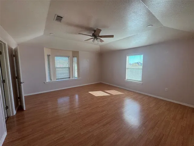 an empty room with wooden floor chandelier fan and windows