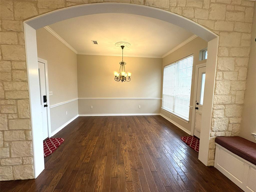 1170 Brazos Loop Gholson, TX 76705 - Photo 14 of 37 Spacious room featuring wood-finish flooring, an arched stone-clad entryway, crown molding, and wainscoting