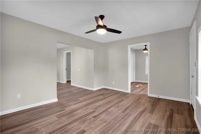 a view of an empty room with wooden floor and a ceiling fan