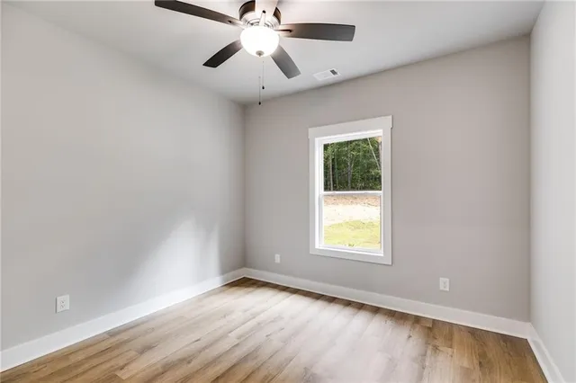 an empty room with wooden floor chandelier fan and windows