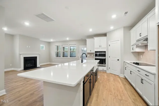 a large kitchen with kitchen island a stove a sink a refrigerator and white cabinets with wooden floor