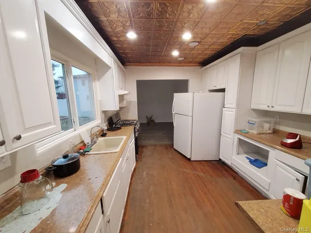 a kitchen with a sink a refrigerator and white cabinets with wooden floor