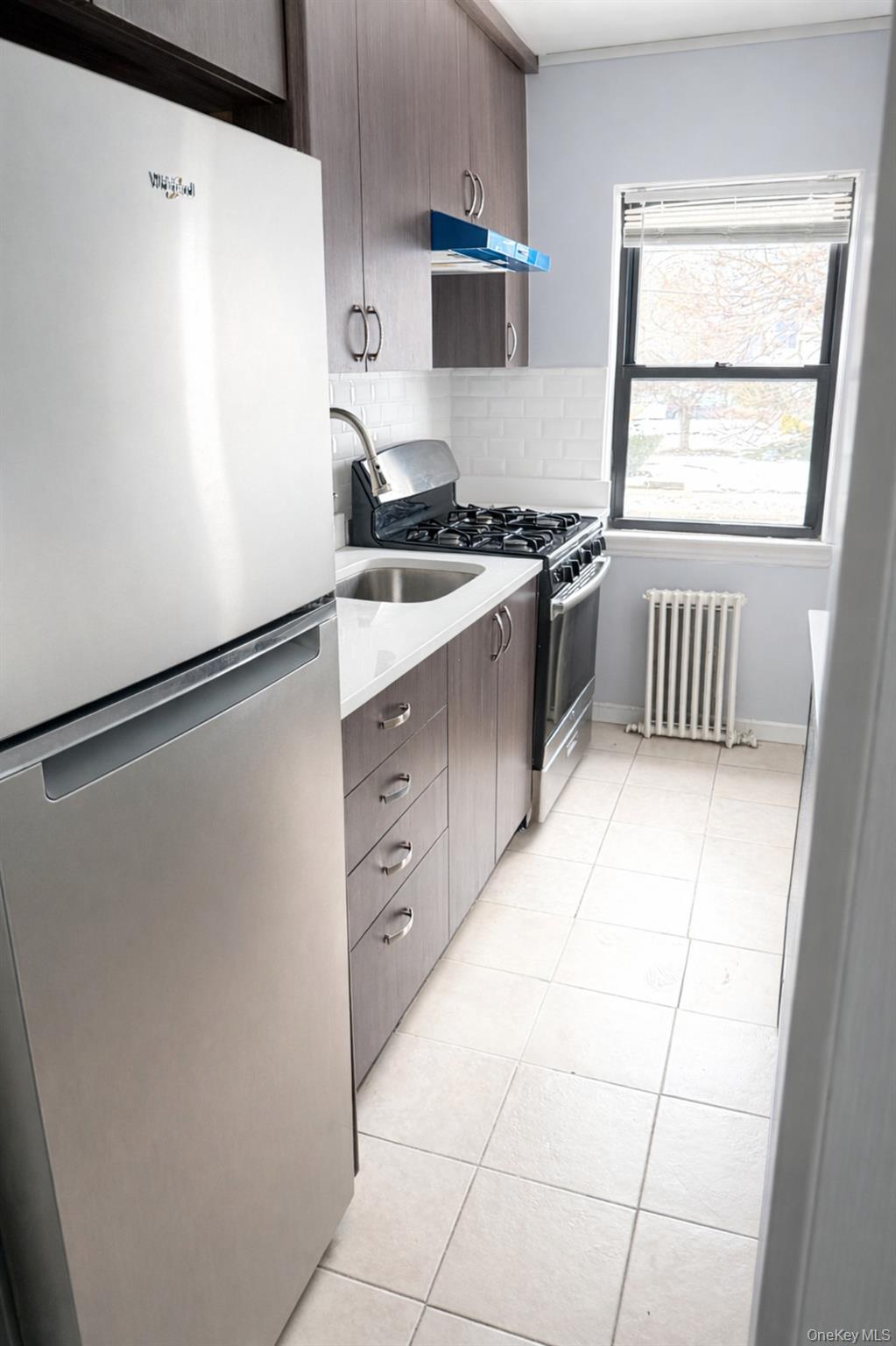 115 Long Beach Road, Unit C Hempstead, NY 11550 - Photo 3 of 9 Kitchen with stainless steel appliances, radiator, light tile patterned flooring, modern cabinets, and under cabinet range hood