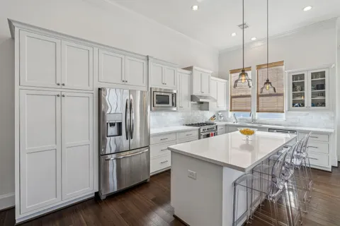 a kitchen with stainless steel appliances granite countertop a refrigerator a sink a stove and white cabinets with wooden floor