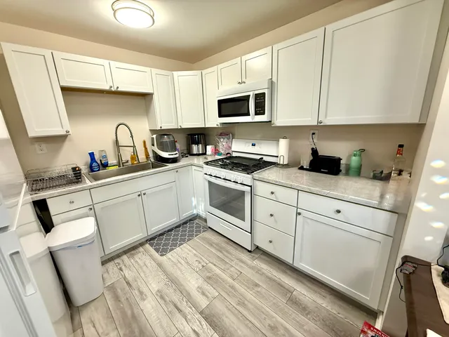 a kitchen with stainless steel appliances granite countertop white cabinets a sink a stove a microwave and a refrigerator