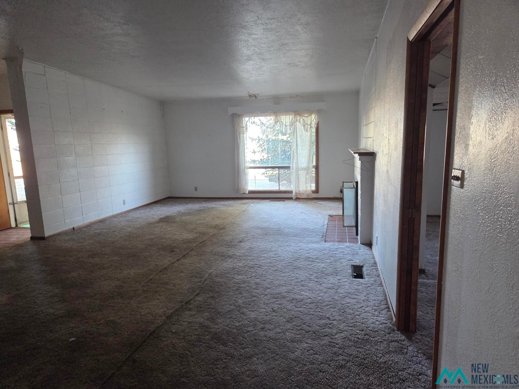 1522 Hogan Street Raton, NM 87740 - Photo 13 of 13 Unfurnished living room with a textured wall, carpet floors, a fireplace, and a textured ceiling