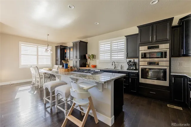 a kitchen with stainless steel appliances granite countertop a stove top oven a sink dishwasher a dining table and chairs with wooden floor