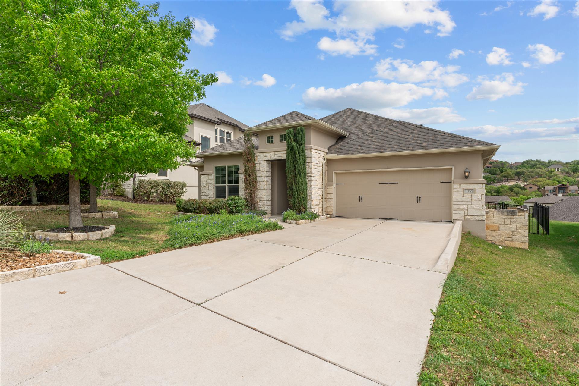 Prairie-style home with stone siding, a front yard, a garage, driveway, and stucco siding